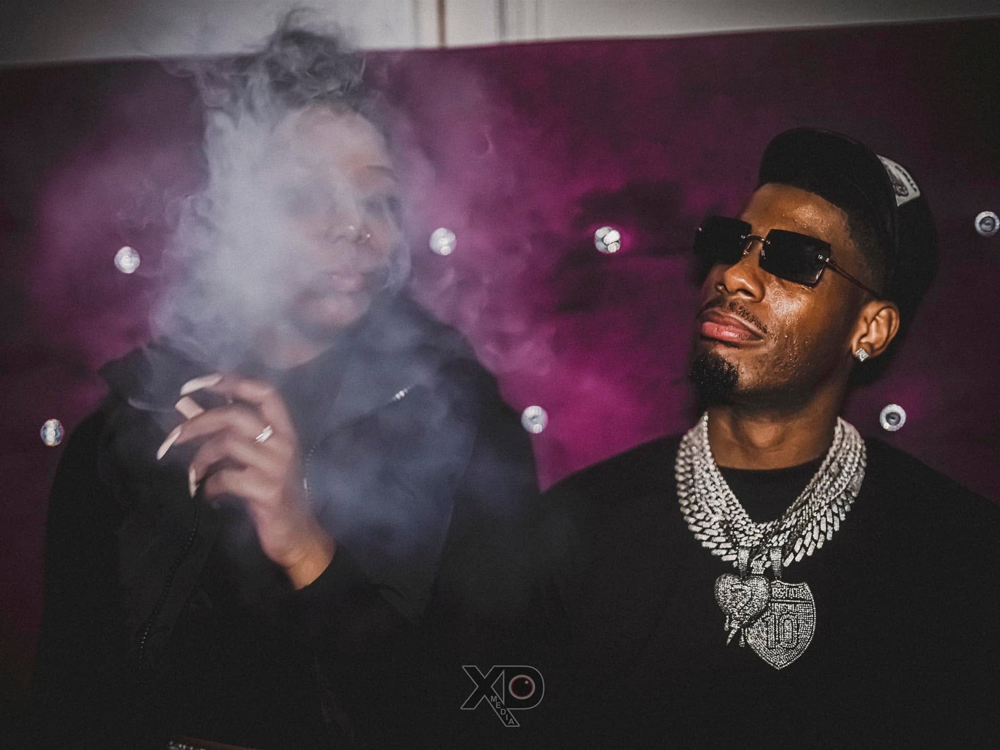 Two people against purple backdrop with smoke