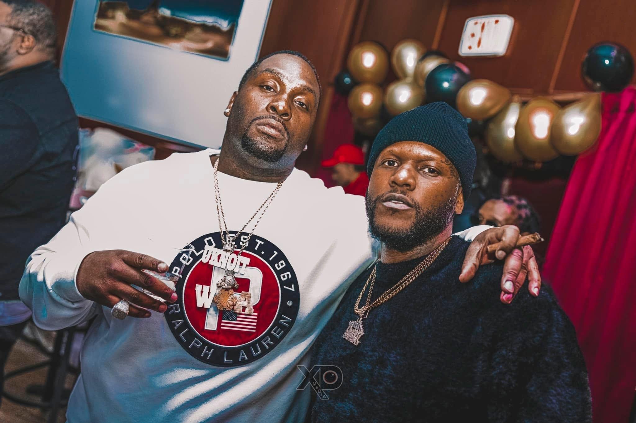 Two men posing at event with gold balloons