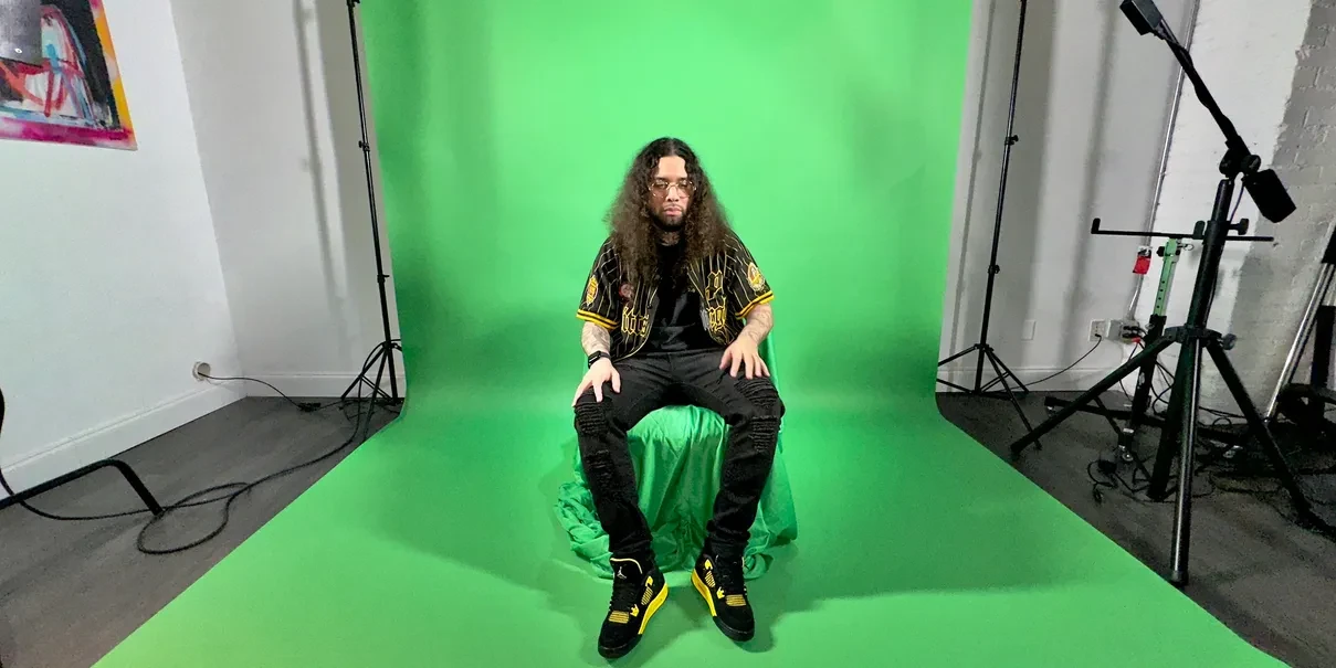 Artist seated in front of green screen backdrop