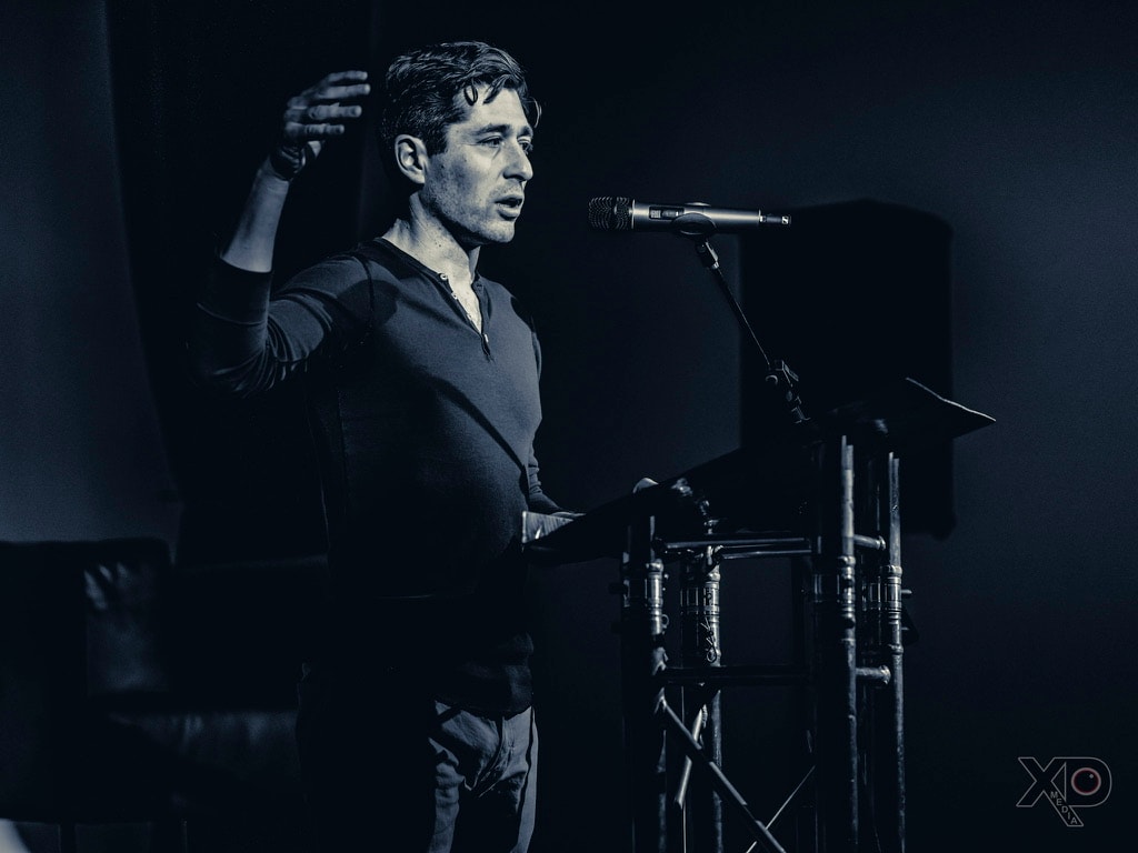 Black-and-white photo of Jacob Frey mid-gesture with one arm raised while speaking at a podium