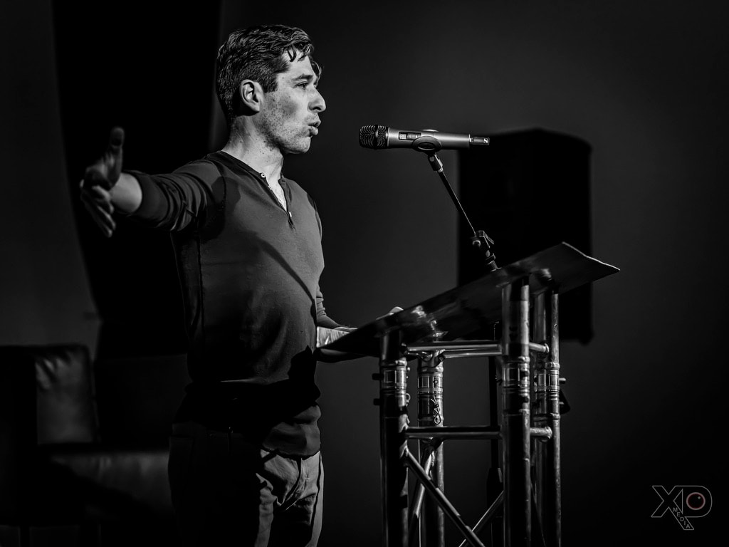 Black-and-white profile shot of Jacob Frey reaching one arm outward while speaking