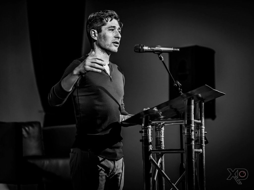 Black-and-white photo of Jacob Frey mid-sentence with one hand raised near his chest