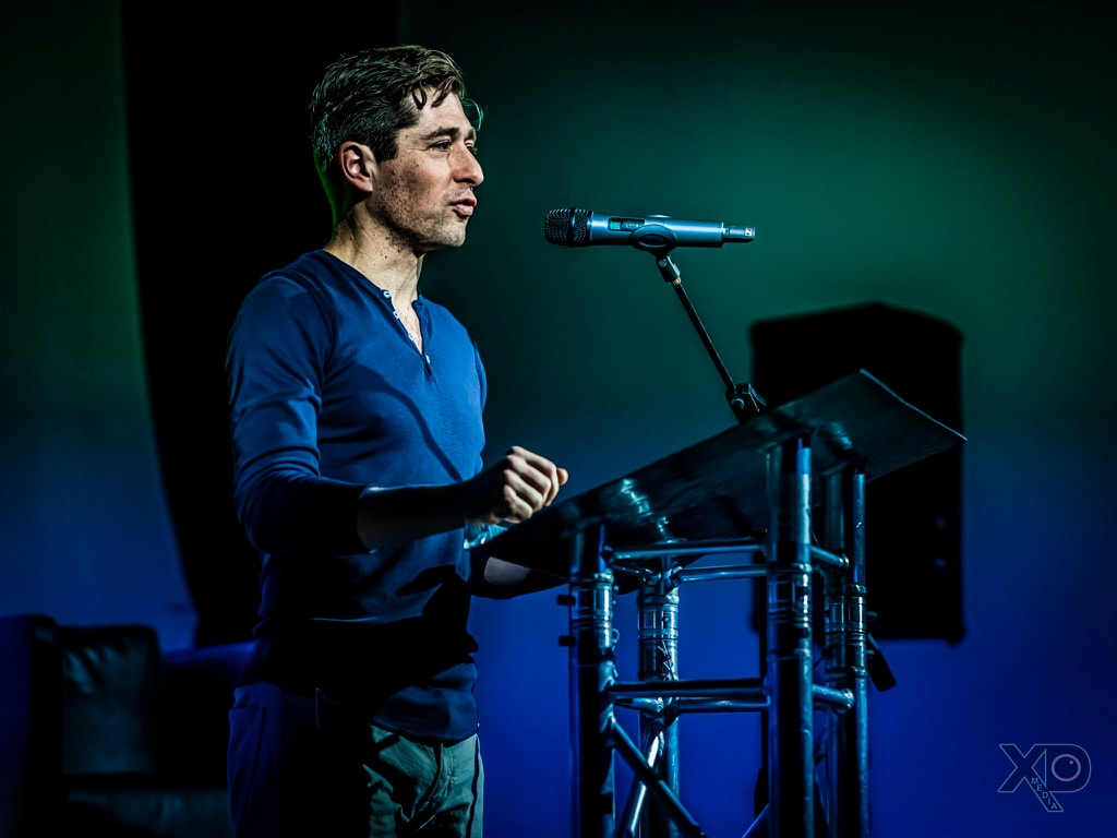 Jacob Frey making a closed-fist gesture while speaking under green-blue stage lighting